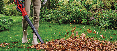 Person using a leaf blower to clear fallen leaves from a lawn in autumn.