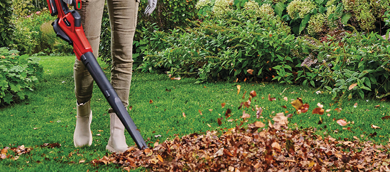 Person using a leaf blower to clear fallen leaves from a lawn in autumn.
